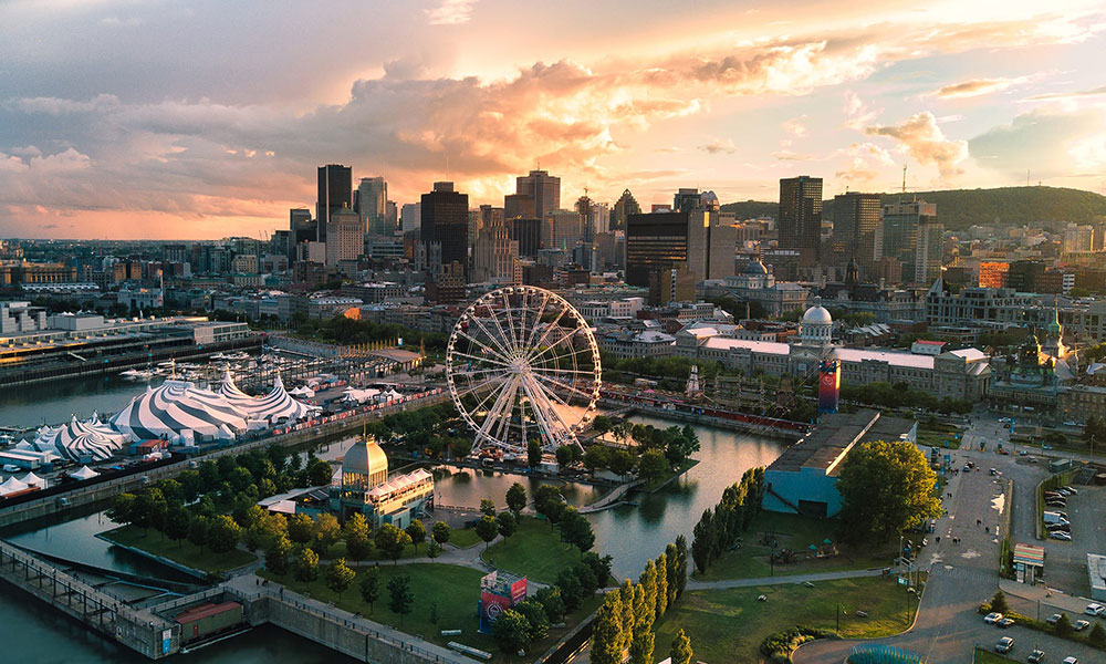 Aerial view of Montreal's Old Port at sunset, with a large Ferris wheel along the waterfront and tents nearby.